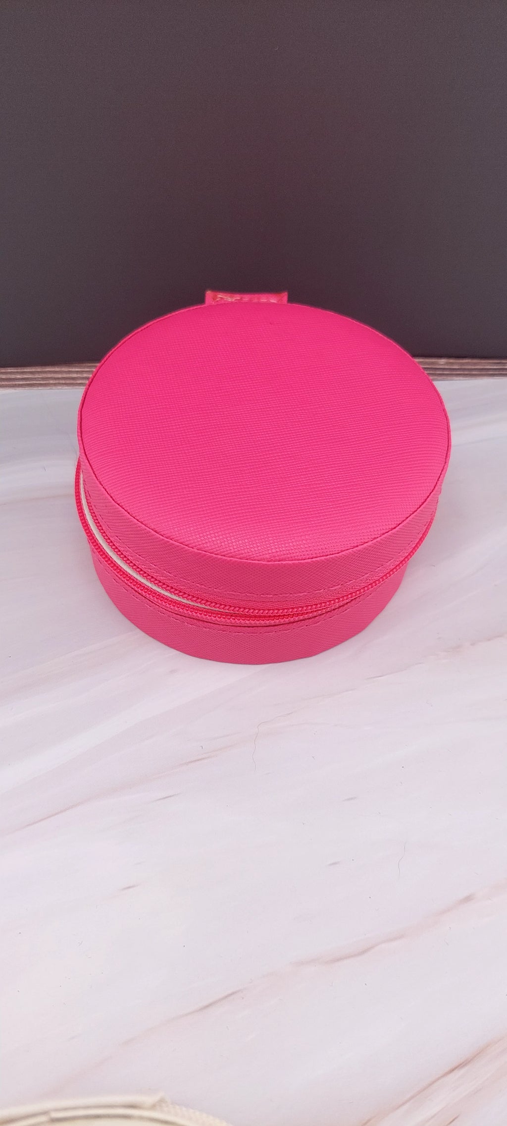 A round jewelry box with a beige interior and patterned exterior, partially open, showing its compartments.