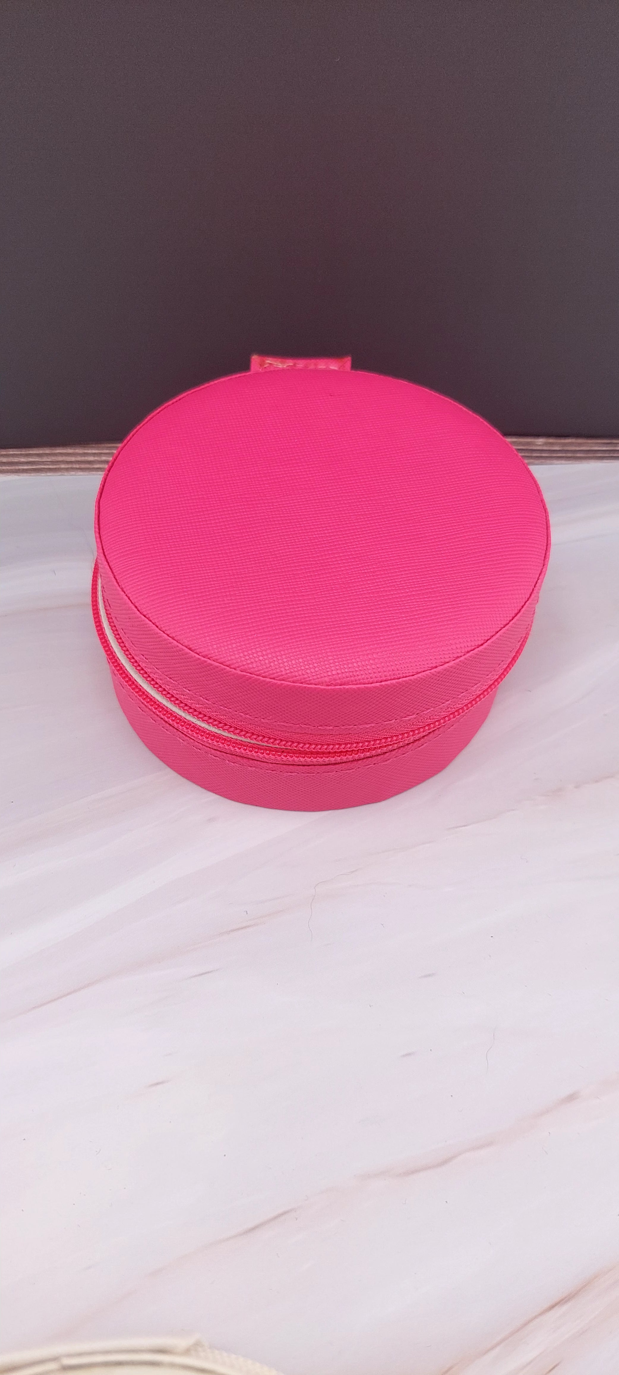 A round jewelry box with a beige interior and patterned exterior, partially open, showing its compartments.