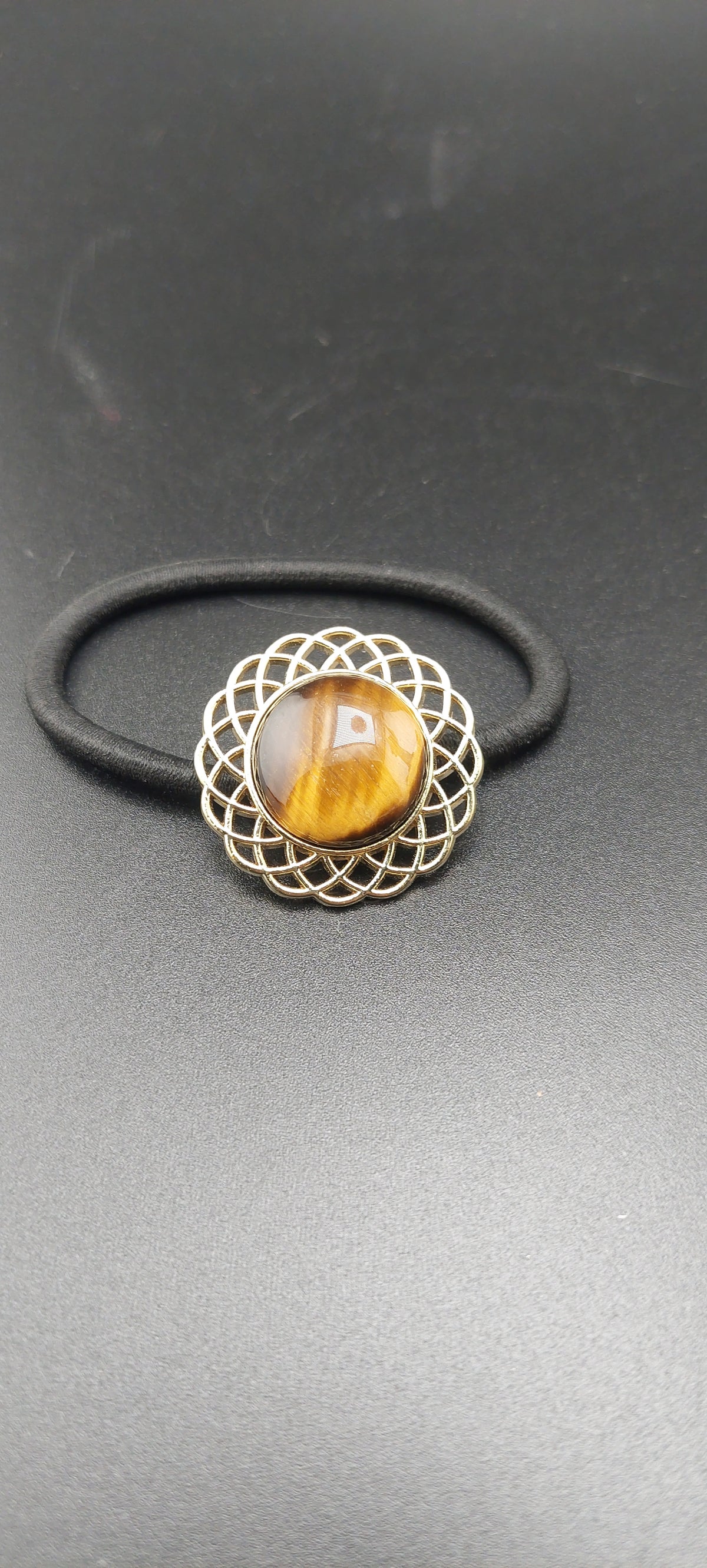 A gold hair tie with a tigers eye stone in the center, presented against a black background.