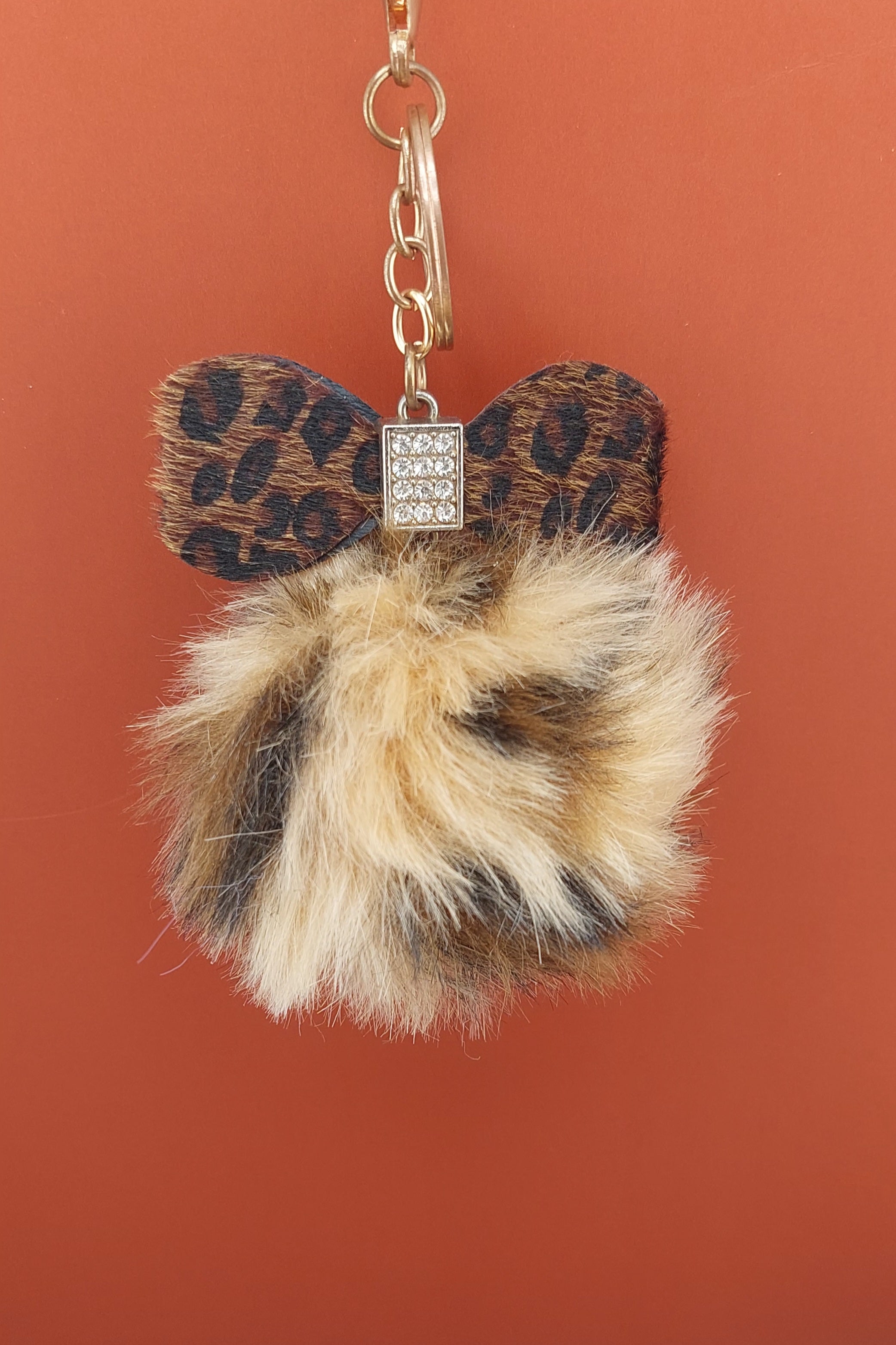 Leopard print bow keychain with fur pom-pom on a brown background