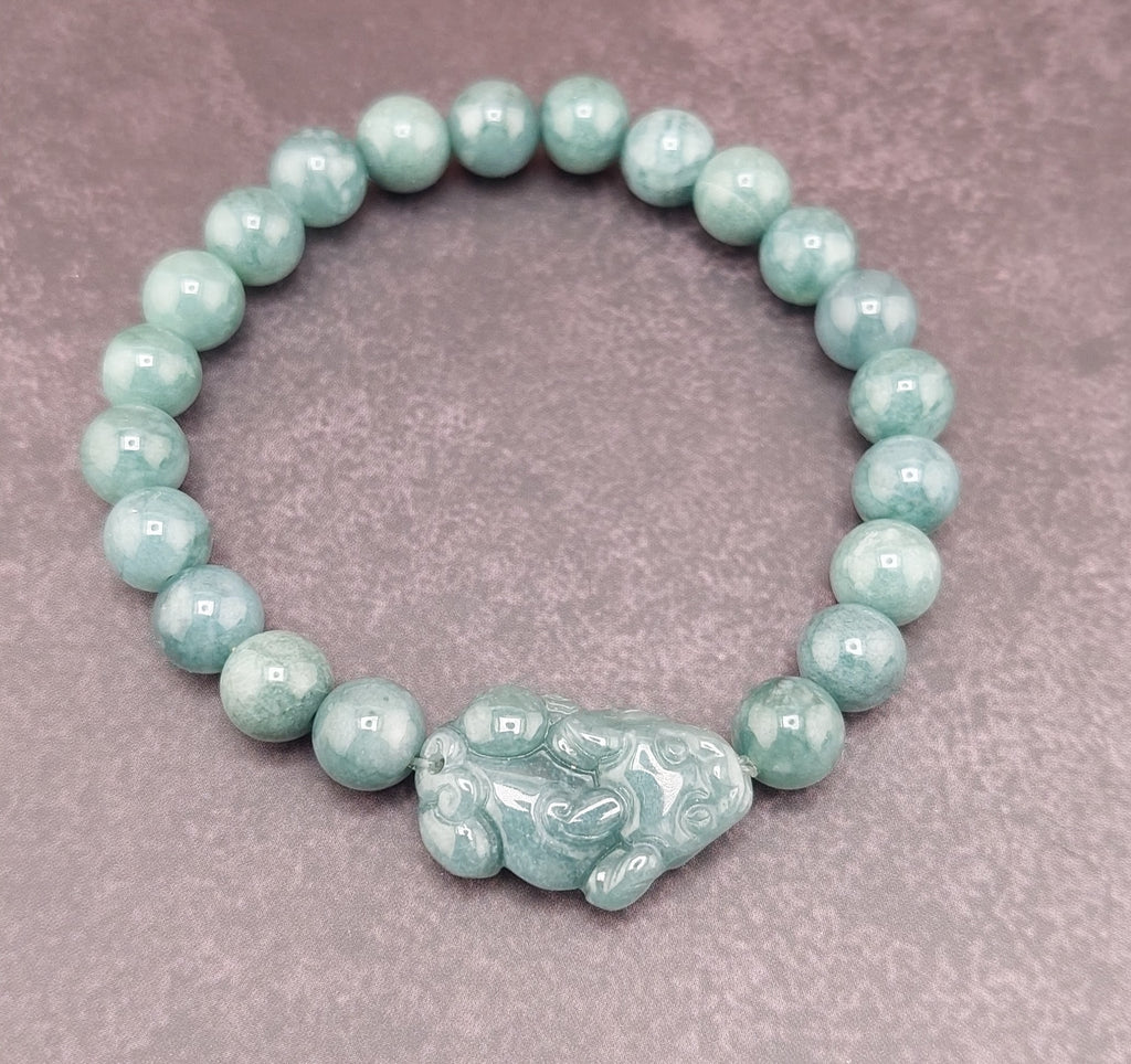 A bracelet made of round blue water jade stones with gold accents and a blue fabric tie at the clasp, featuring a small circular silver charm.