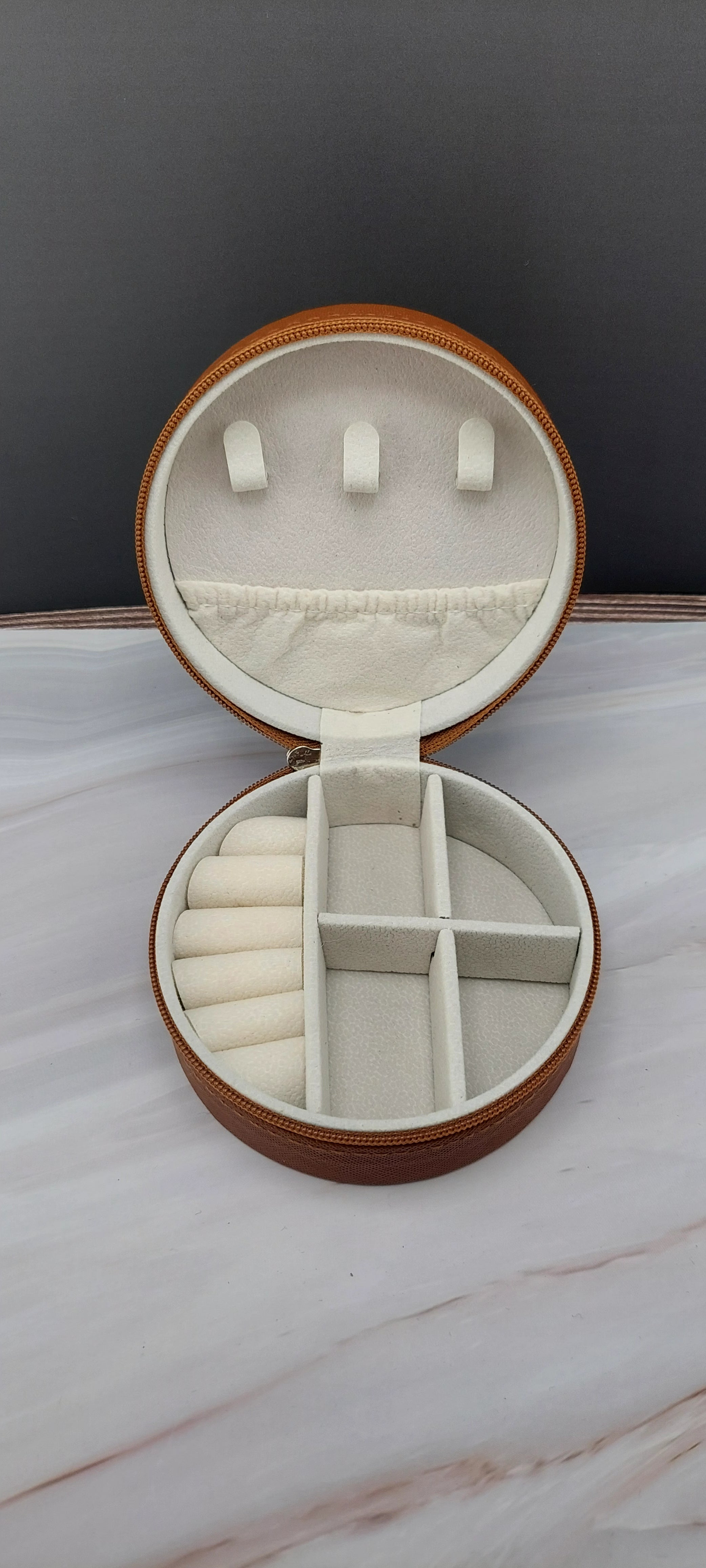 A round jewelry box with a beige interior and patterned exterior, partially open, showing its compartments.