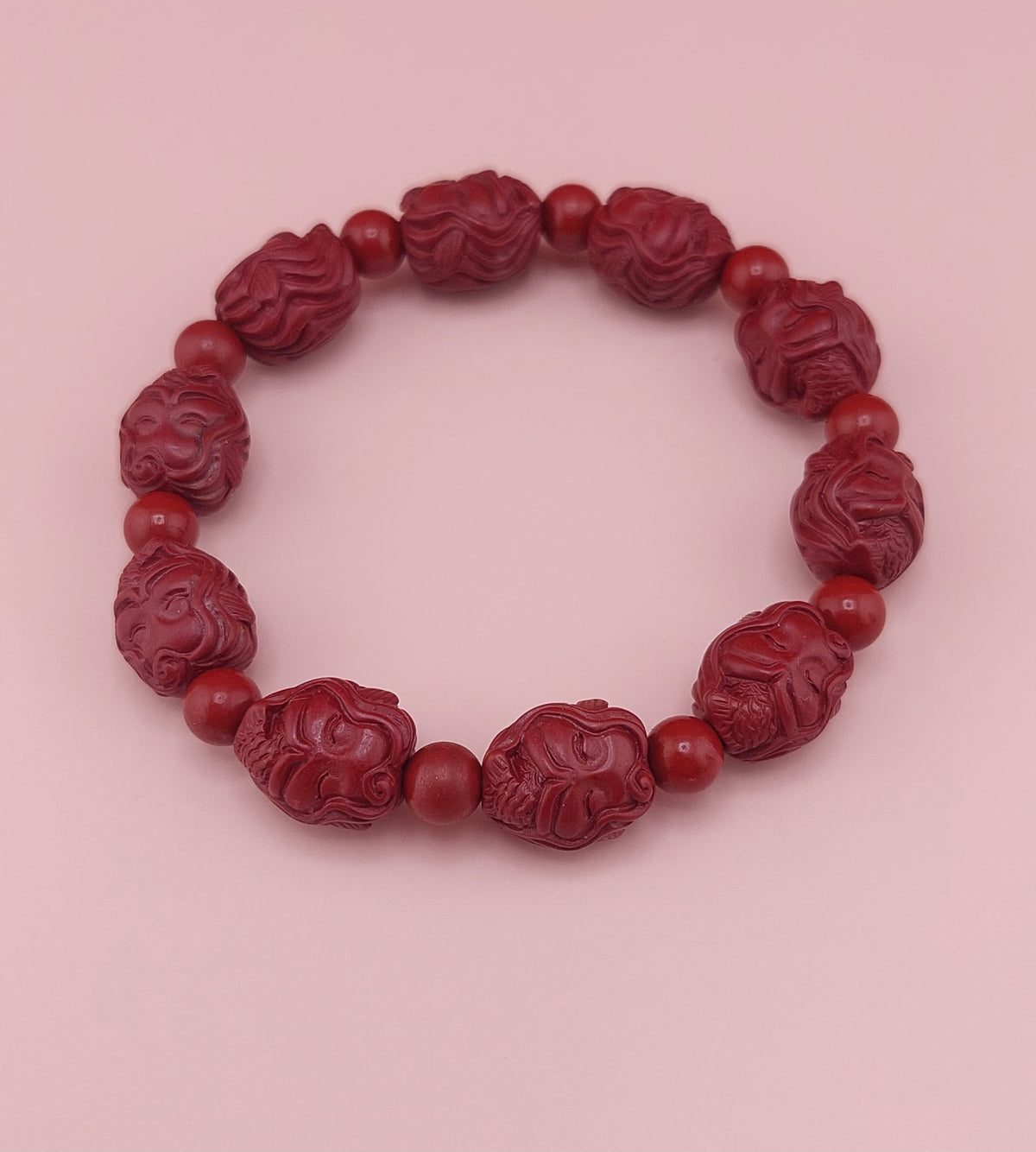 A red cinnabar bracelet with mermaid character designs on the beads, displayed against a pink background.