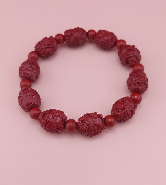 A red cinnabar bracelet with mermaid character designs on the beads, displayed against a pink background.