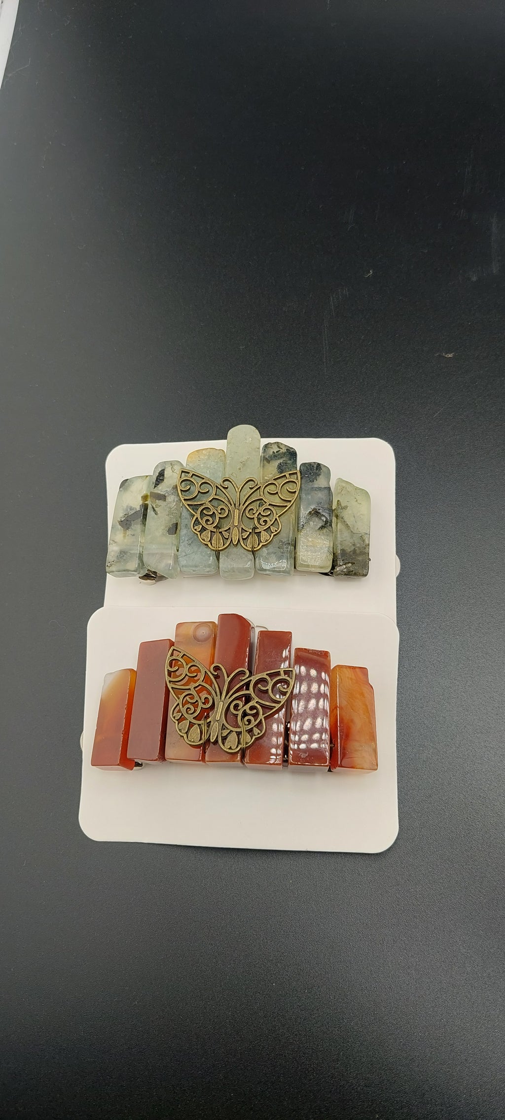 A set of Butterfly Stone Hair Clips displayed on a stand, with various colors and designs, including gold and silver tone butterflies on top of each clip.