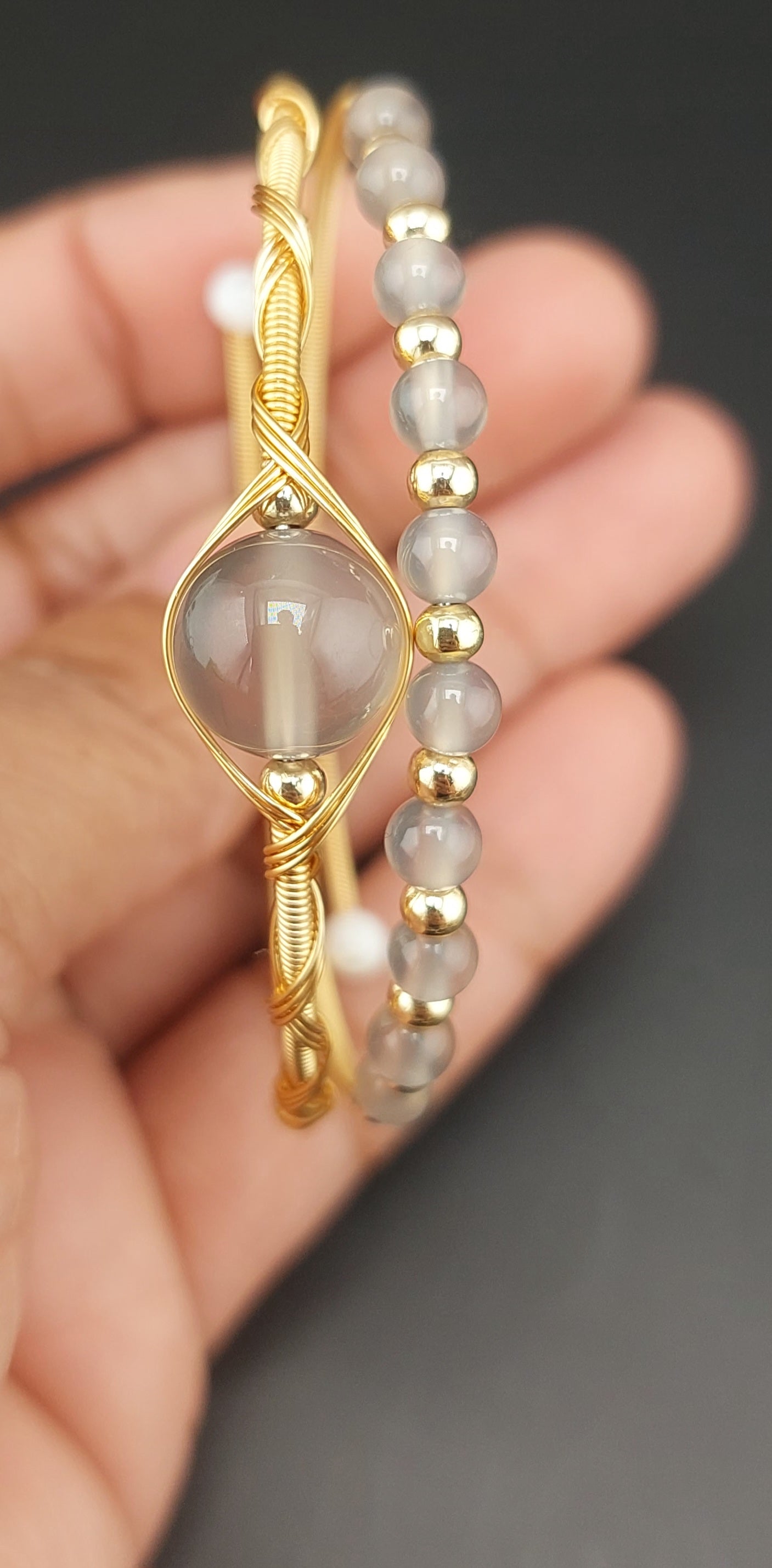 Gold and gray beaded bracelet held in a hand against a dark background