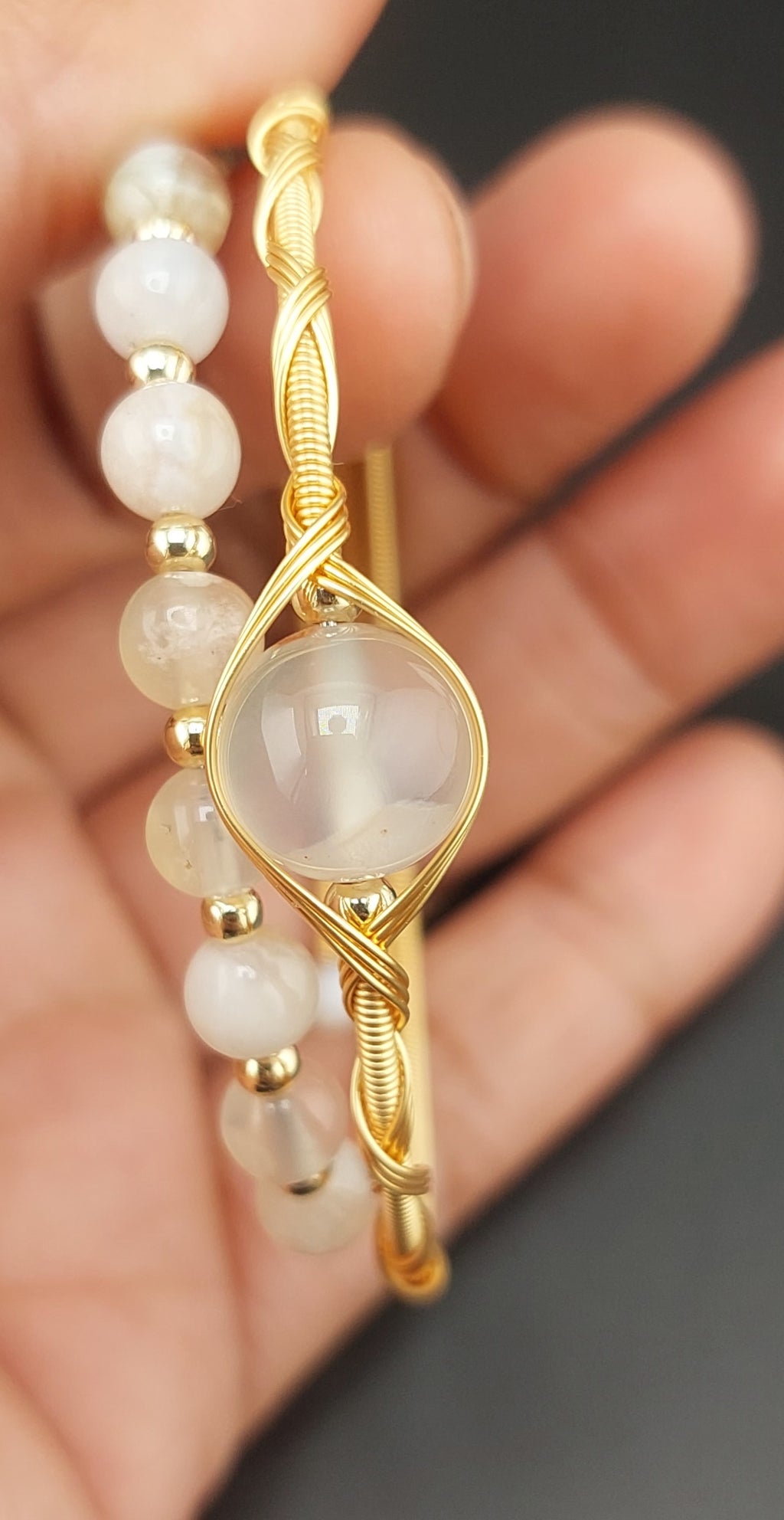 Gold bracelet with a central stone and pearl-like beads on a blurred hand background