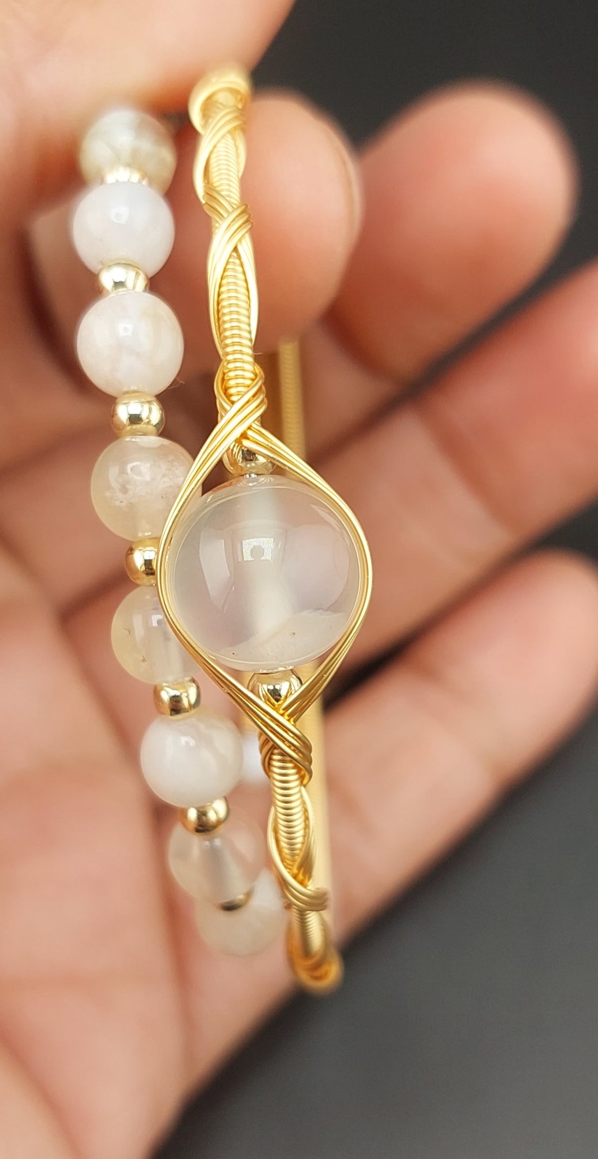 Gold bracelet with a central stone and pearl-like beads on a blurred hand background