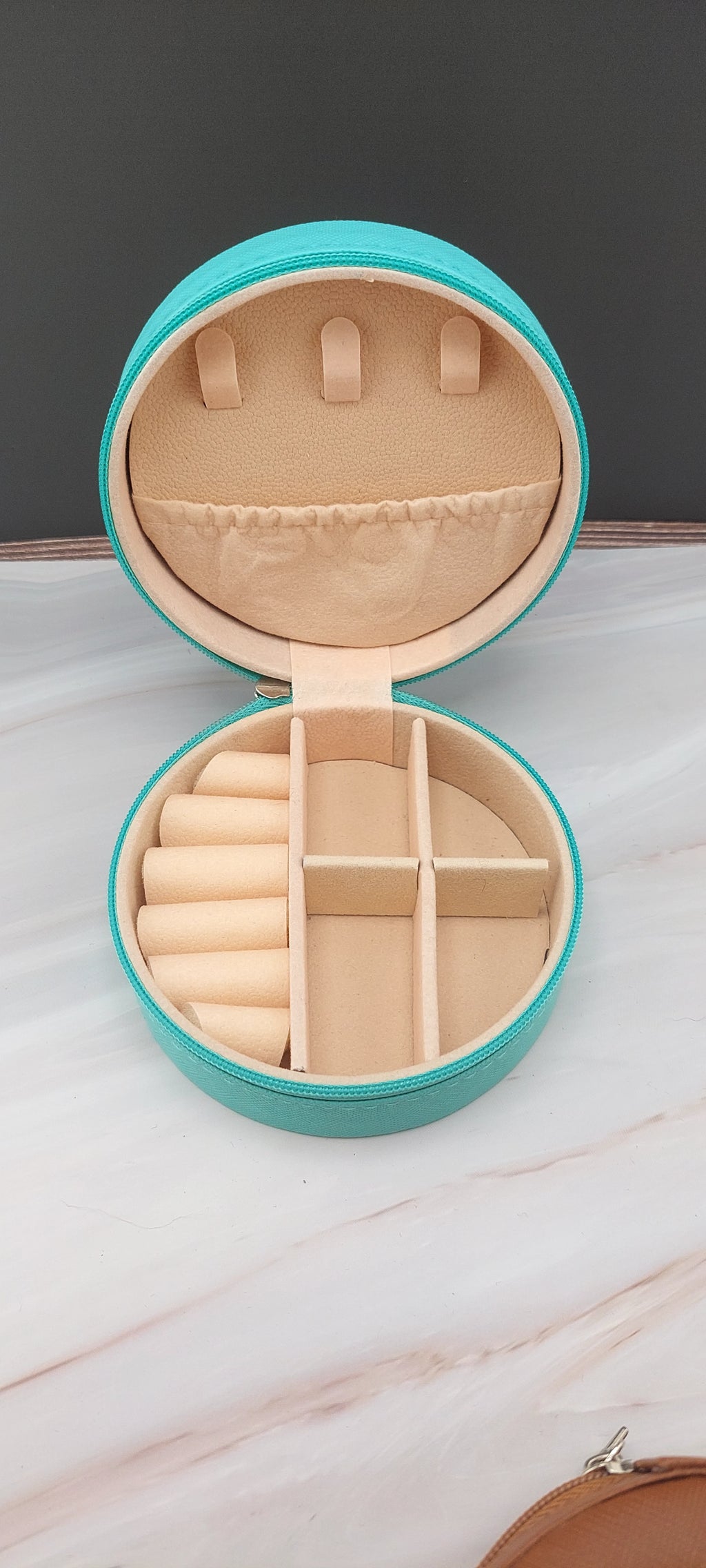 A round jewelry box with a beige interior and patterned exterior, partially open, showing its compartments.