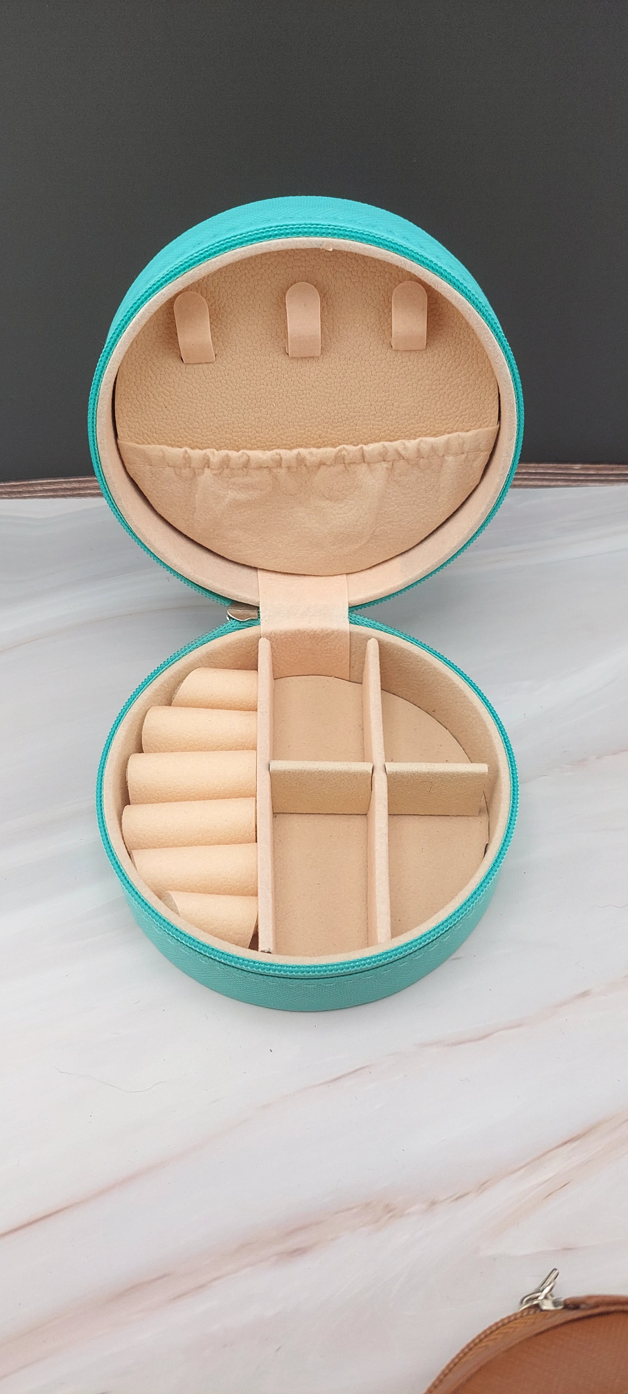 A round jewelry box with a beige interior and patterned exterior, partially open, showing its compartments.