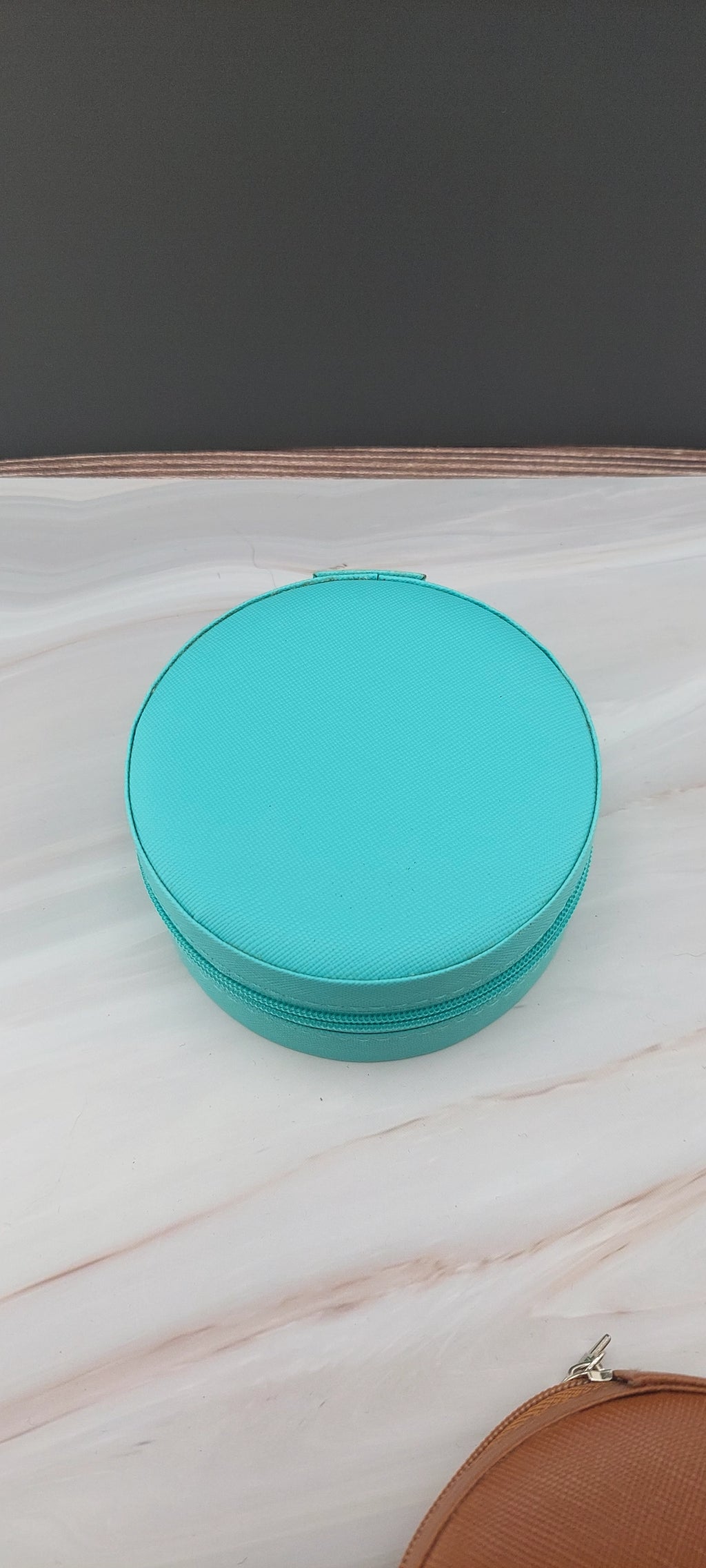 A round jewelry box with a beige interior and patterned exterior, partially open, showing its compartments.