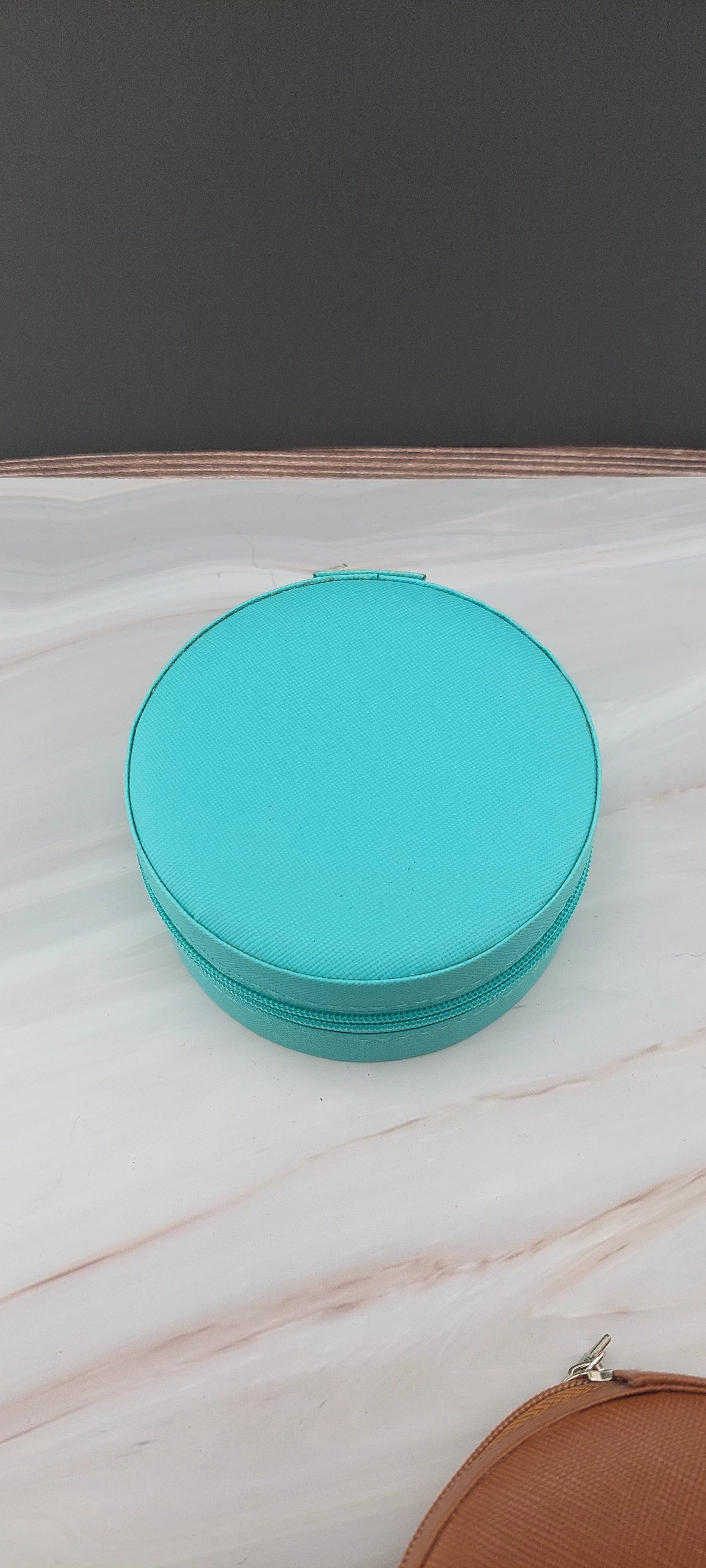 A round jewelry box with a beige interior and patterned exterior, partially open, showing its compartments.