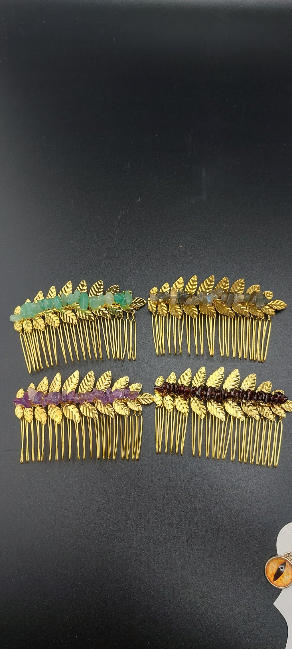 A collection of gold leaf hair clips with various colored stones attached to them, displayed against a dark background.