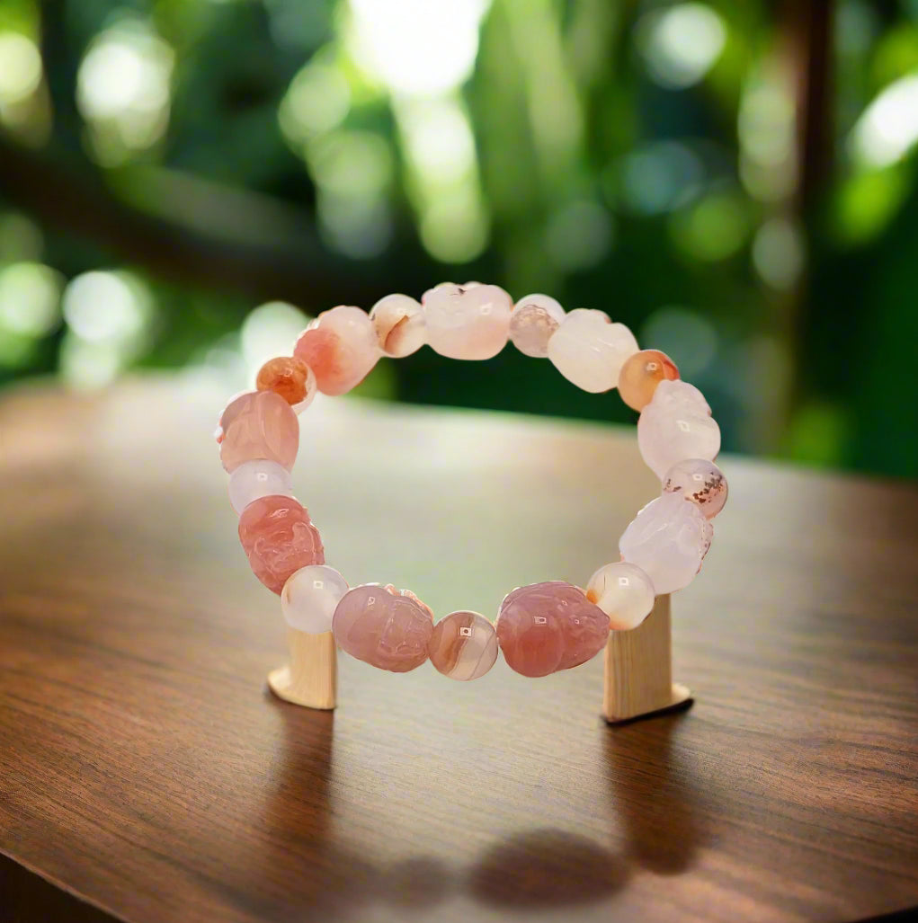 A Yuanyuan Agate Pixui bracelet displayed on a wooden surface with a blurred greenery background.