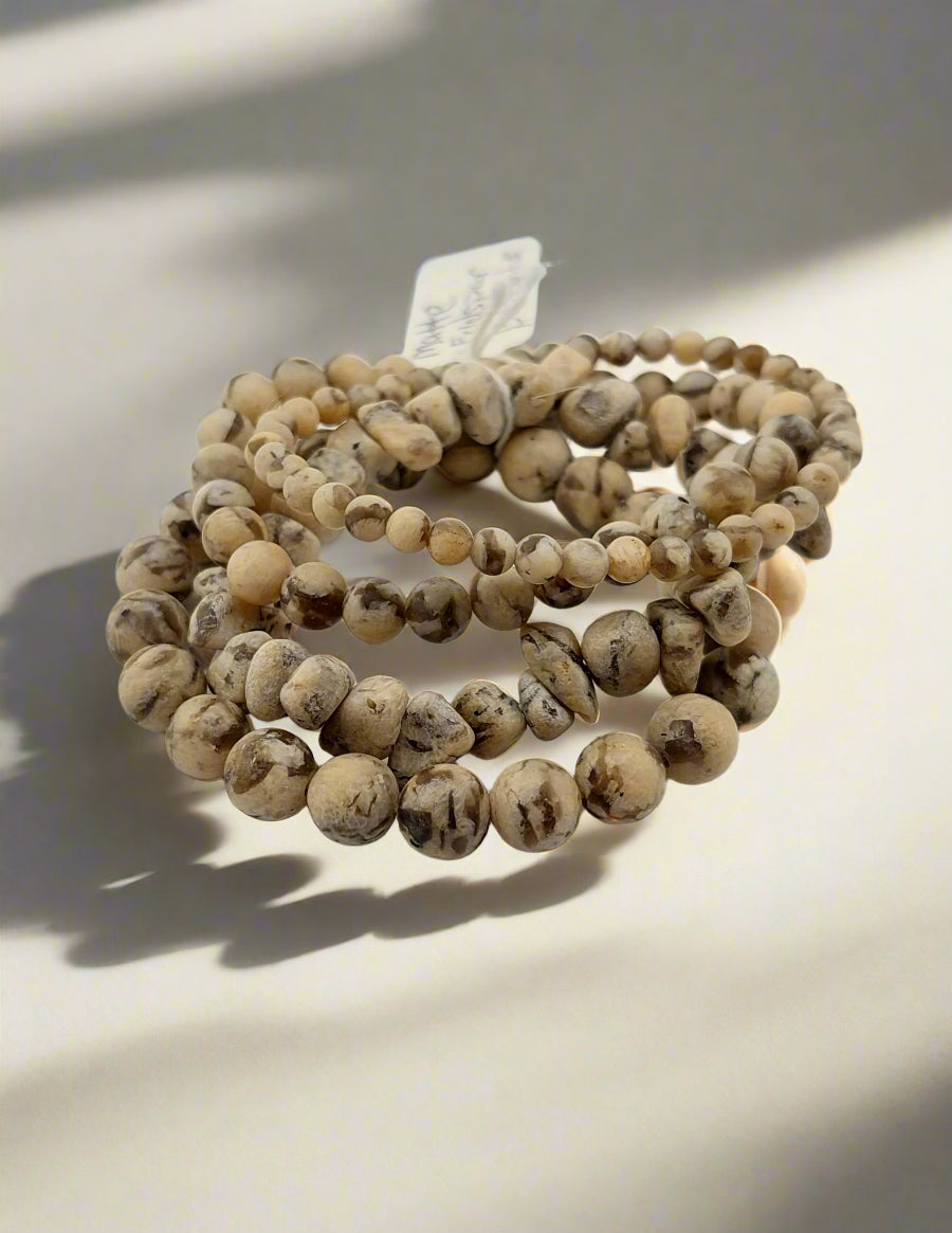 A stack of picture jasper bracelets displayed on a flat surface with natural lighting.